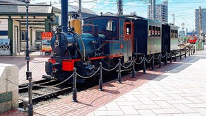 A vintage steam locomotive on display, surrounded by a chain barrier, with overhead electrical wires and a clear sky in the background. - Comfort Hotel Matsuyama (Matsuyama)