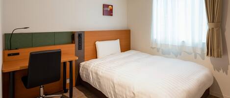 A hotel room with a bed, a desk with a chair, and a window with curtains.