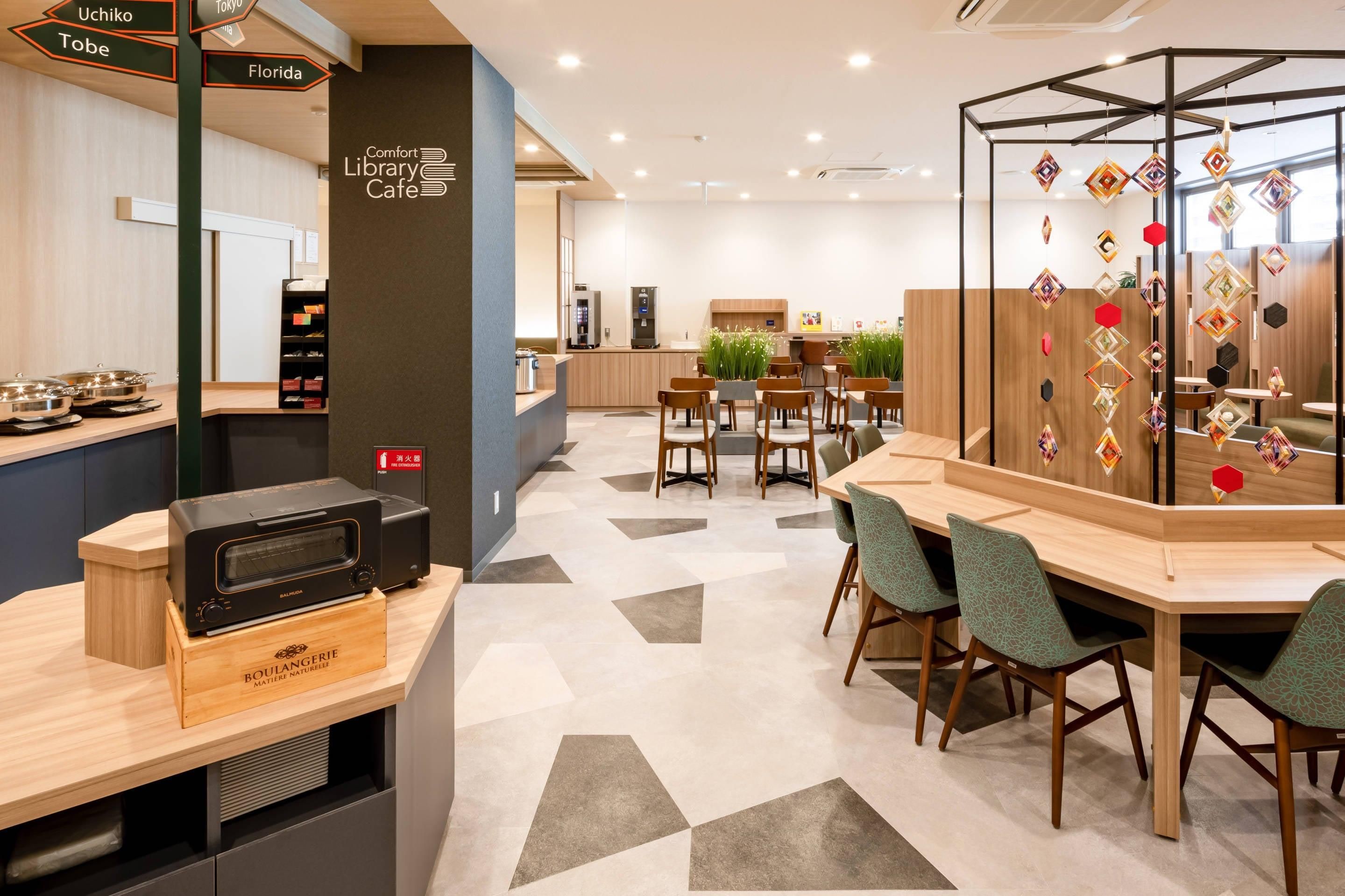 A modern library cafe with a central seating area, a kitchenette, and a decorative wall with hanging ornaments.