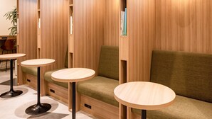 Un espace de détente moderne, doté de cloisons en bois, de bancs rembourrés de couleur verte et de tables rondes en bois.