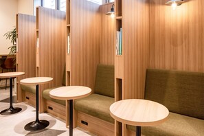 Un área de descanso moderna con separadores de madera, bancos acolchados verdes y mesas redondas de madera.