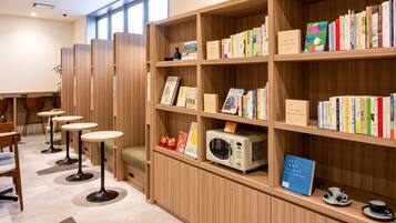 A library with wooden bookshelves, a microwave, and tables with chairs.