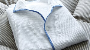 A neatly folded white garment with blue trim and buttons, placed on a striped bedspread. - Comfort Hotel Matsuyama (Matsuyama)