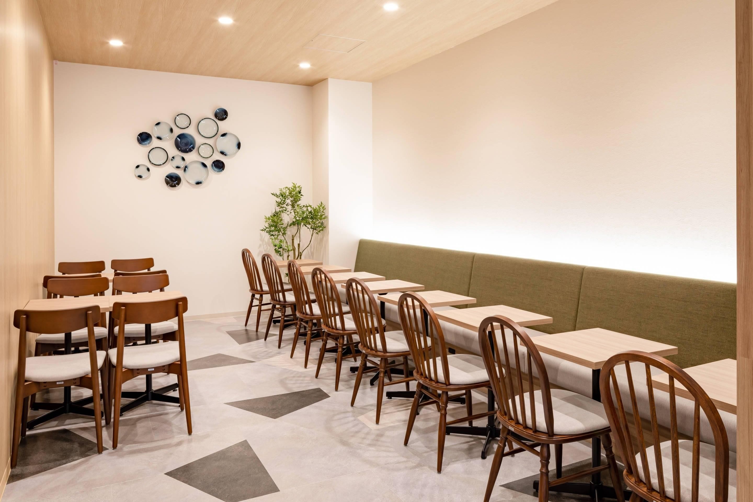 Un comedor con sillas y mesas de madera, un adorno en la pared y una planta.