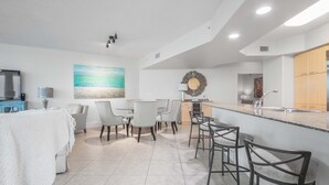 Eine moderne Küche mit einer zentralen Kochinsel, einem Essbereich mit Stühlen und einer Wohnbereich mit Sofa und Fernseher.