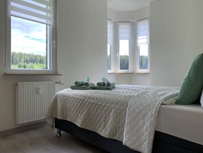 Quarto com cama, radiador e janelas com persianas.