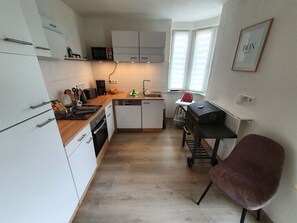 Uma cozinha compacta com armários brancos, micro-ondas, cafeteira e um pequeno espaço de refeições com uma cadeira.