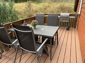 En træterrasse med et bord, stole, grill og en potteplante.
