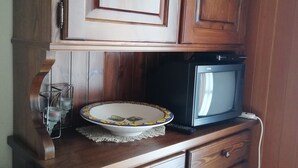 A wooden cabinet with a microwave on top, a decorative plate, and a small candle holder.