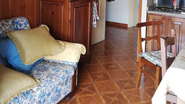 A cozy living room with a sofa, wooden wardrobe, and a dining area with a chair and table.