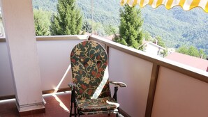 A balcony with a chair and a table, a view of a mountain, and a yellow-striped awning.