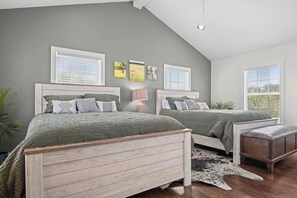 A bedroom with two beds, a wooden headboard, a nightstand, a lamp, and a cowhide rug. - Mighty Oaks Retreat | 2BR Farmhouse w/ Fire Pit (D'Hanis)