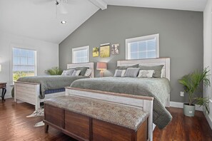 A bedroom with two beds, a wooden bench, and a nightstand. - Mighty Oaks Retreat | 2BR Farmhouse w/ Fire Pit (D'Hanis)