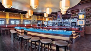 Zona de bar con varios taburetes, una barra y lámparas colgantes.