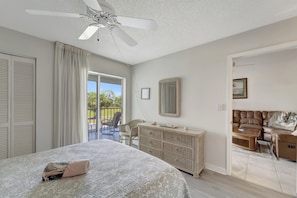 A bedroom with a bed, a dresser, a ceiling fan, a large mirror, and a view of the outdoors.