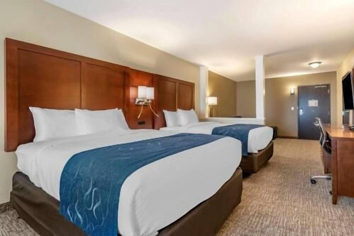 A hotel room with two beds, a wooden headboard, a desk, and a lamp.