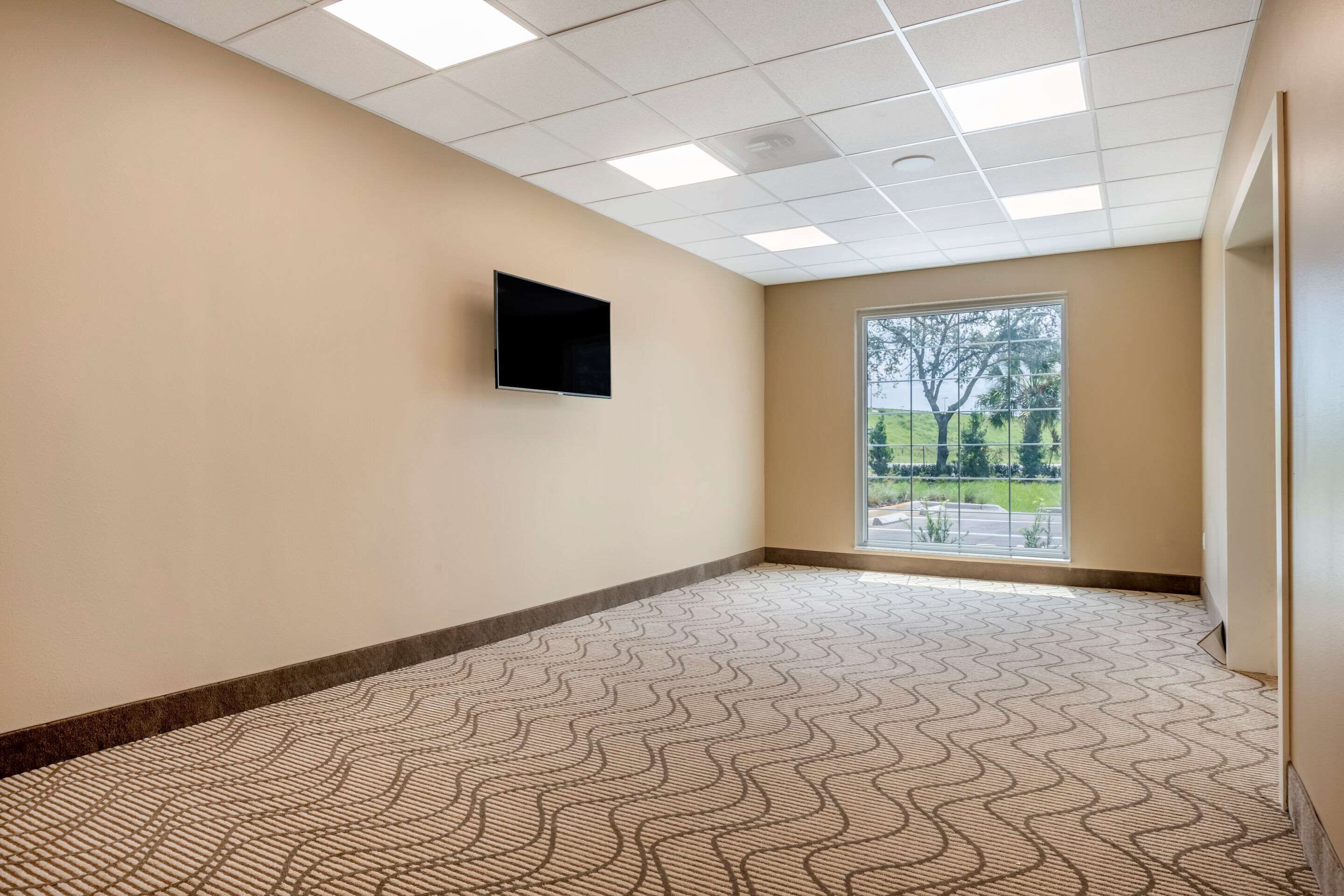 A hallway with patterned flooring, a mounted TV, and a window with a view of greenery.