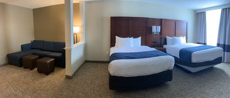 A hotel room with two beds, a sofa, and a small seating area.