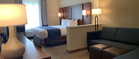 A hotel room with a bed, a desk with a lamp, a sofa, and a headboard with wall-mounted lamps.