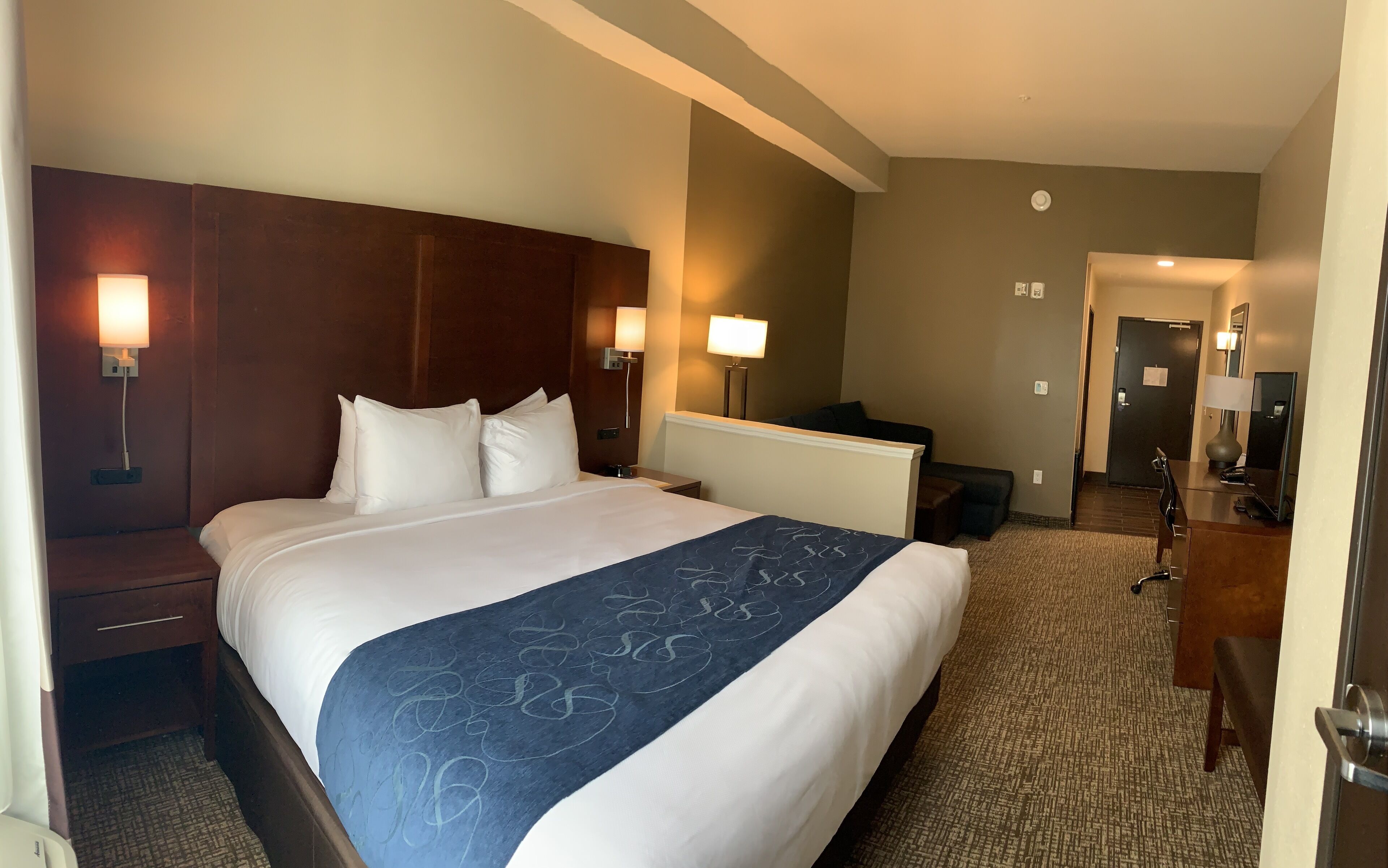 A hotel room with a large bed, bedside lamps, a desk, and a chair.