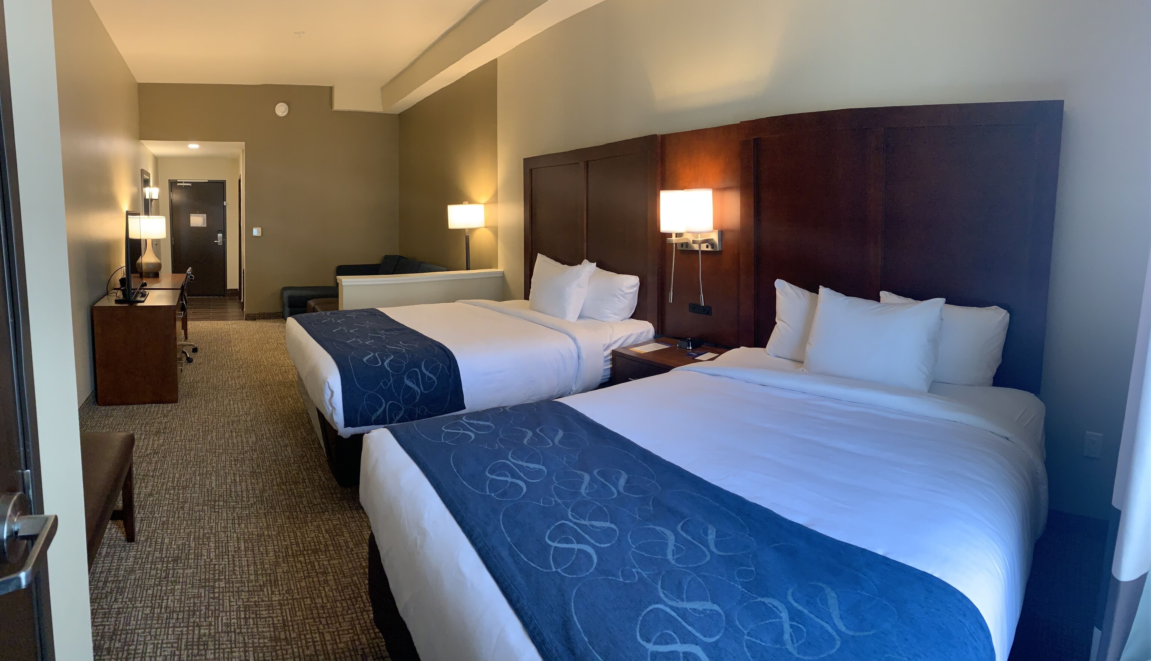 A hotel room with two beds, a desk, a chair, and a small table.