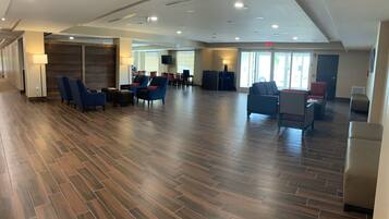 A spacious lobby with a wooden floor, several seating areas, and a reception desk.