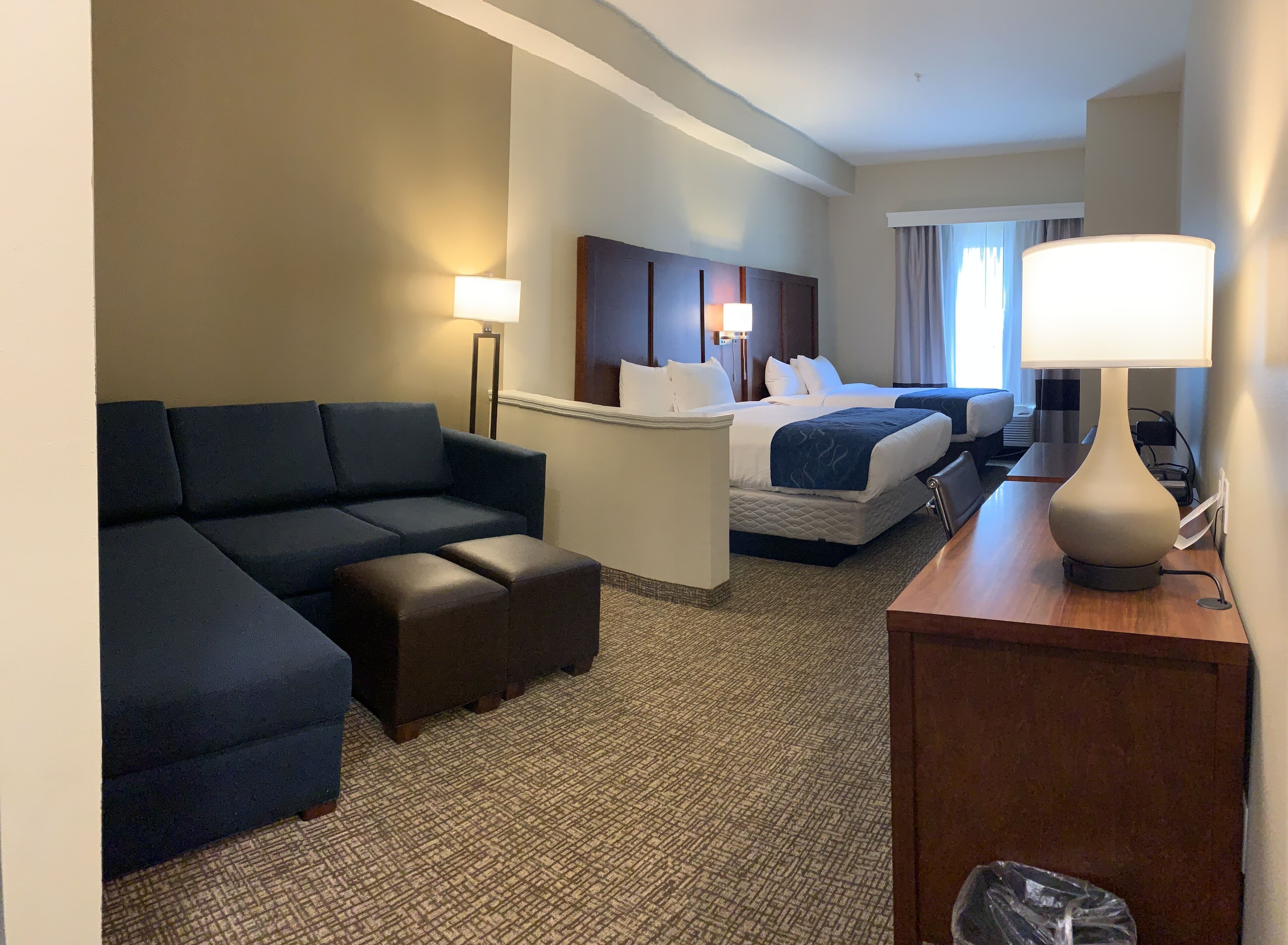 Ein Hotelzimmer mit einer Couch, zwei Betten, einem Schreibtisch und einer Lampe.
