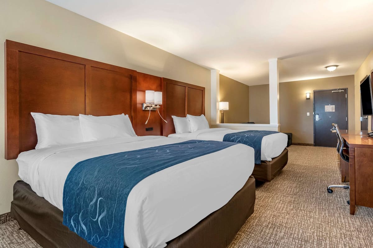 A hotel room with two beds, a wooden headboard, a desk, and a television.