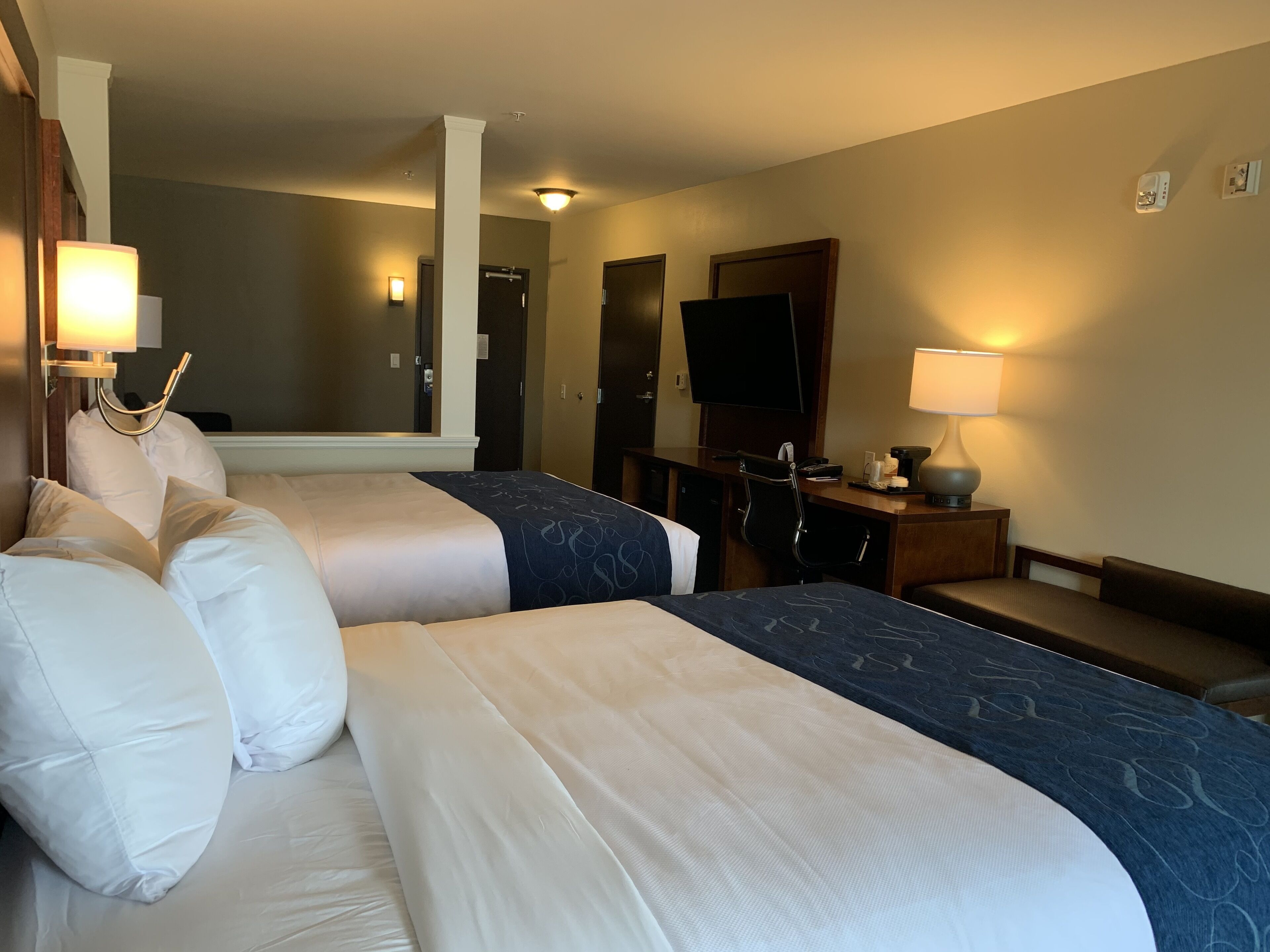 Une chambre d’hôtel avec deux lits, un bureau, une chaise, une télévision et un miroir.
