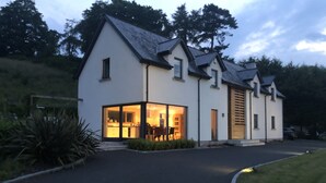 Een modern huis met een grote glazen voorgevel, een oprit en een verzorgd gazon.