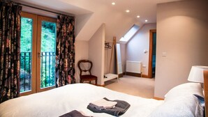 Een slaapkamer met een groot bed, een stoel, een klein tafeltje en een raam met gordijnen.