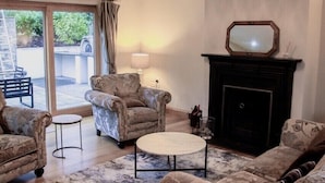Een woonkamer met een open haard, gestreept meubilair, een kroonluchter en uitzicht door een glazen deur.