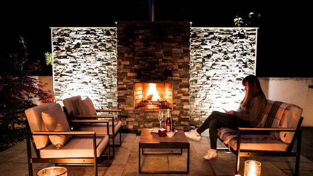 Een terras met een stenen openhaard, twee comfortabele stoelen, een bijzettafeltje en kaarsen.