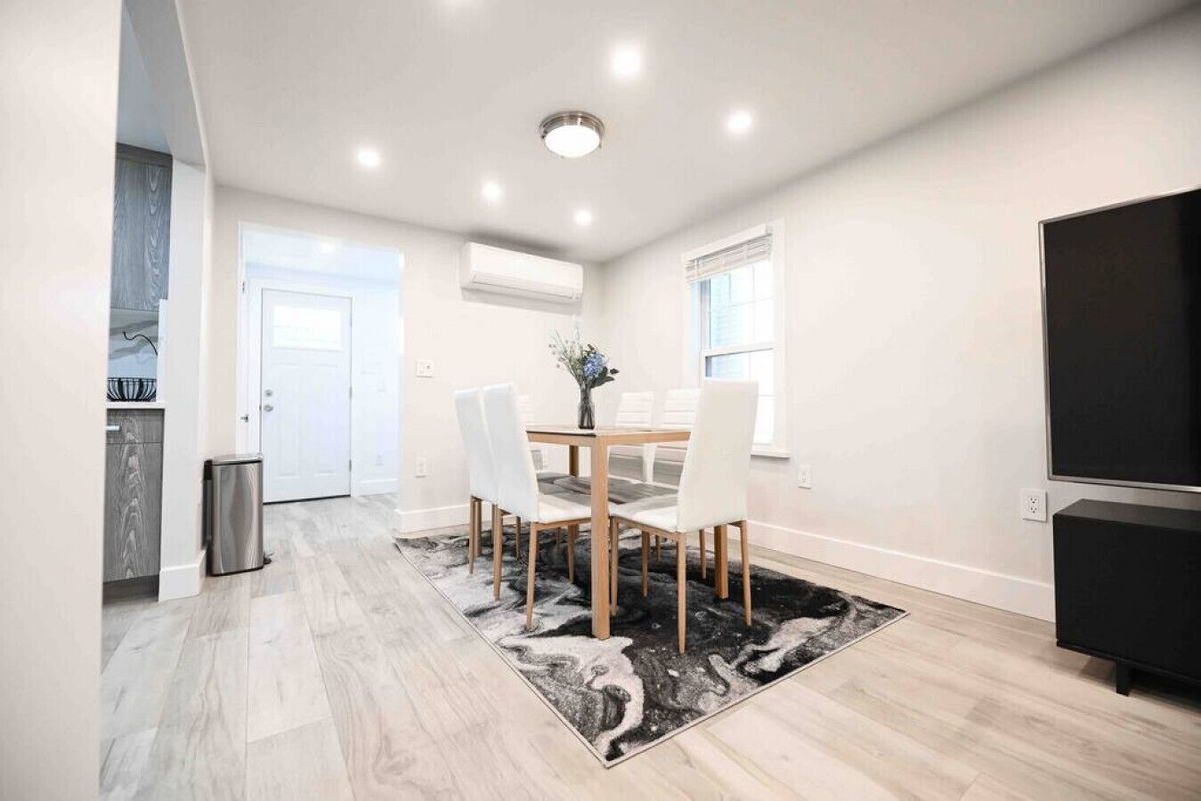 Un espace repas moderne avec une table et des chaises en bois, un tapis noir et blanc et un meuble TV noir.