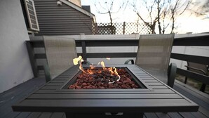 Una parrilla cuadrada al aire libre con fuego encendido sobre una terraza de madera.