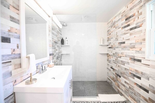 Un baño moderno con un tocador blanco, un espejo grande y una zona de ducha.