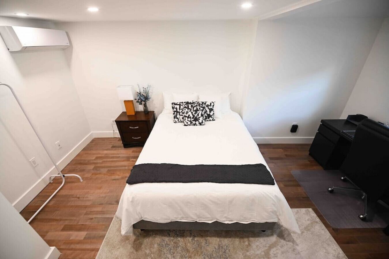 A bedroom with a bed, a nightstand, a lamp, and a desk.