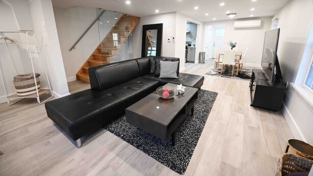 Una sala de estar moderna con un sofá de cuero negro, una mesa de centro y un mueble para televisión. Se ve una escalera que conduce a otro nivel.