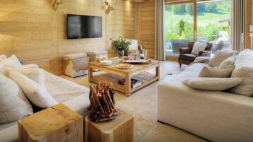 Een gezellige woonkamer met houten inrichting, een flatscreen televisie aan de wand en een groot raam met uitzicht op de natuur.