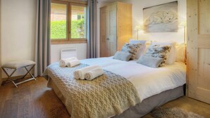 Un dormitorio con una cama grande, un armario de madera, un taburete pequeño y una ventana con cortinas.