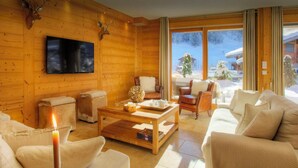 Interior acogedor de una cabaña de troncos con chimenea, sillones de cuero, una mesa de centro de madera y un amplio ventanal con vistas a un paisaje nevado.