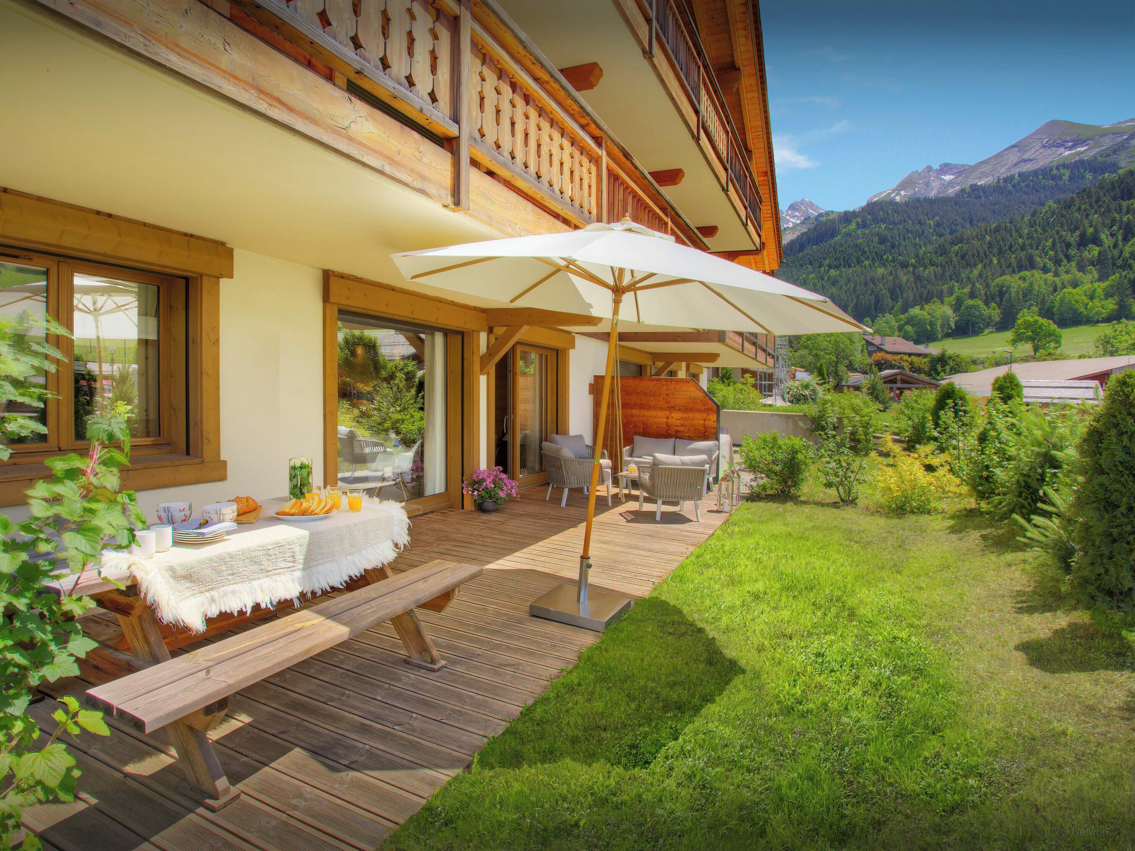 Une terrasse en bois avec des meubles d’extérieur, un patio couvert et une vue sur un paysage montagneux.
