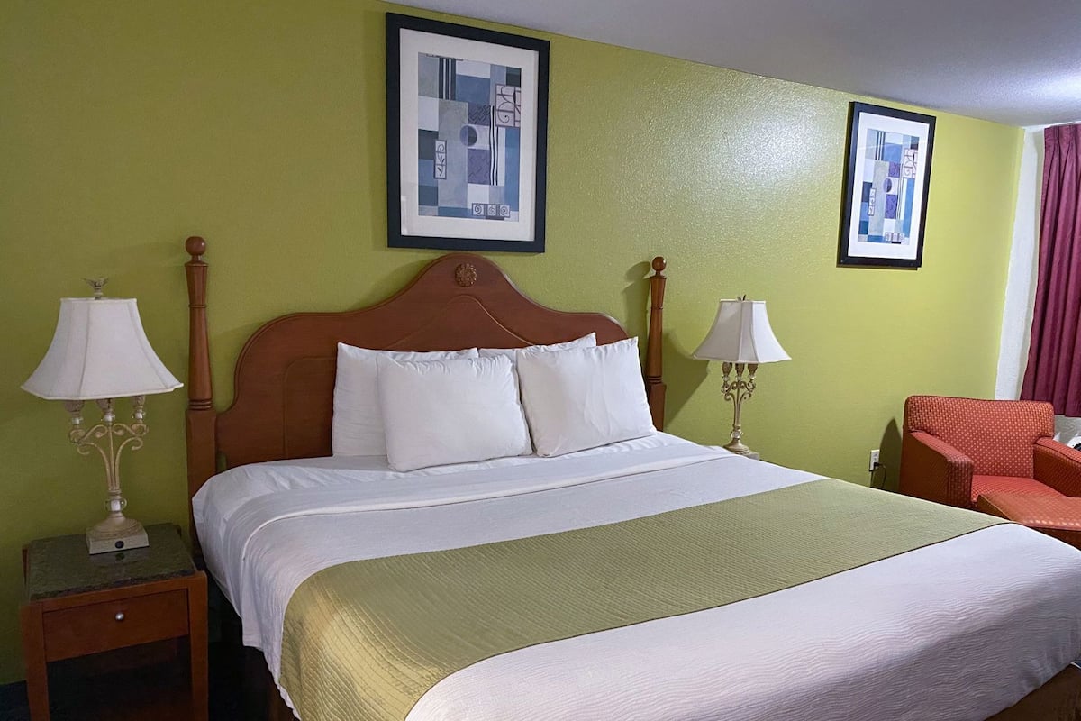 A hotel room with a large bed, two bedside tables with lamps, a chair, and two framed pictures on the wall.