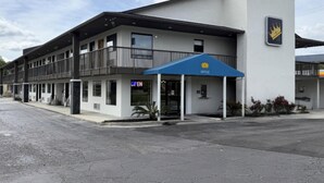 Un hôtel avec un auvent bleu, une enseigne indiquant qu’il est ouvert et un logo en forme de couronne sur le bâtiment.