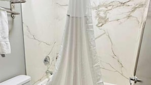Une salle de bain avec des toilettes blanches, une baignoire avec un rideau de douche et des murs en marbre.