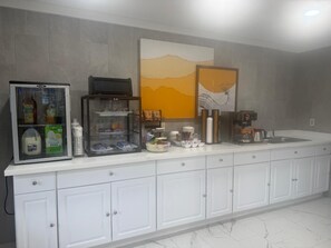 Une cuisine équipée d’un réfrigérateur, d’une machine à café et de divers produits alimentaires disposés sur le plan de travail.
