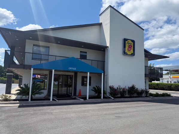 Un edificio moderno con un toldo azul que indica 'OFFICE' y un letrero que señala un hotel Super 8.