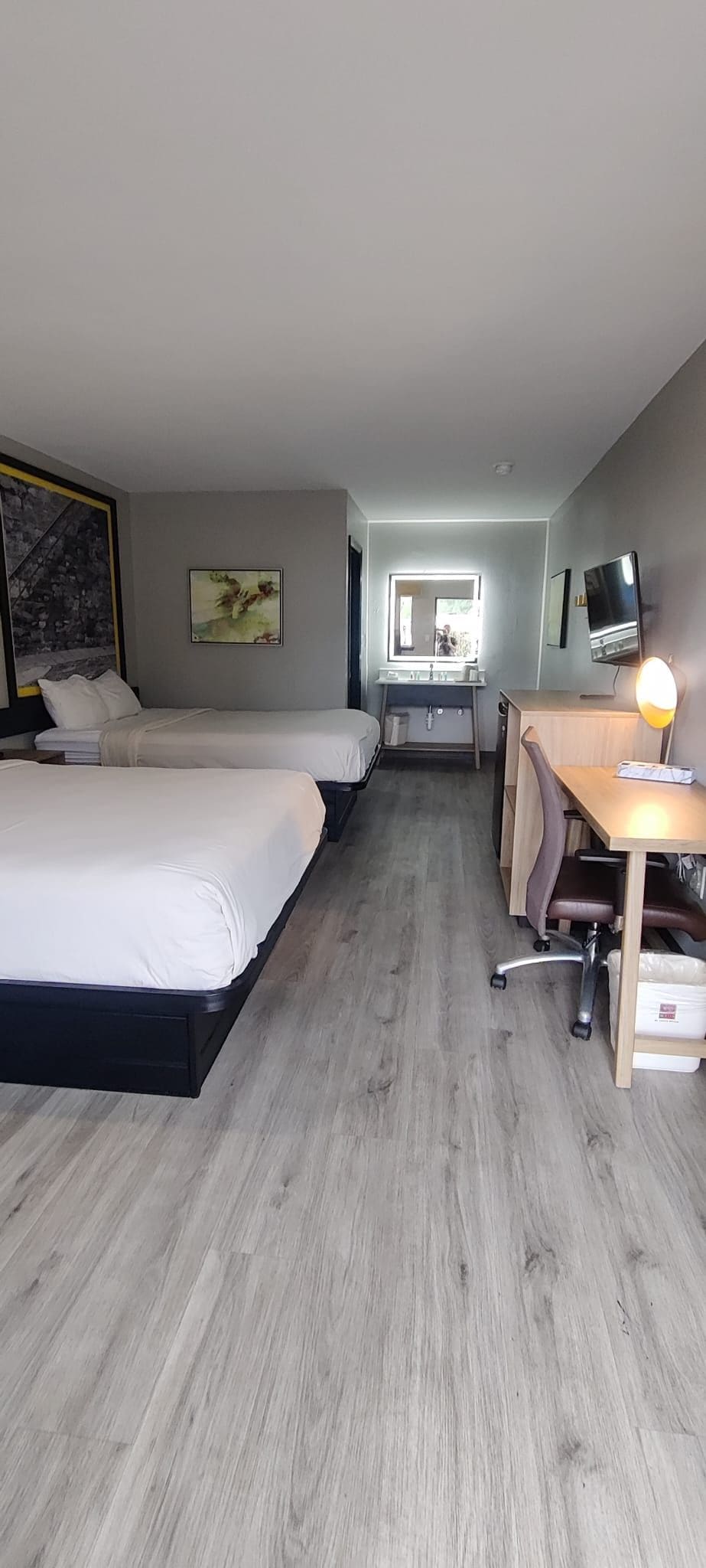 A hotel room with two beds, a desk, a chair, a TV, and a window.