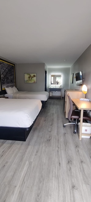 Une chambre d’hôtel avec deux lits, un bureau, une chaise, une télévision et une fenêtre.