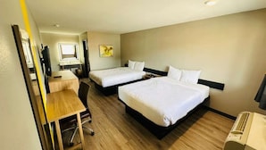 Une chambre d’hôtel avec deux lits, un bureau, une chaise, une petite table, une fenêtre et un climatiseur fixé au mur.